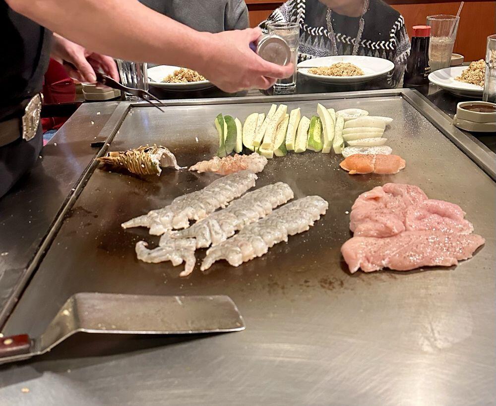 Hibachi chef grilling premium proteins and vegetables at Jinbeh teppanyaki table